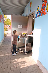 Ein Junge hilft beim Transport des Essenswagens