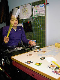Mädchen im Rollstuhl schlägt so schnell wie möglich mit einer Fliegenklatsche auf eine Memory-Karte.